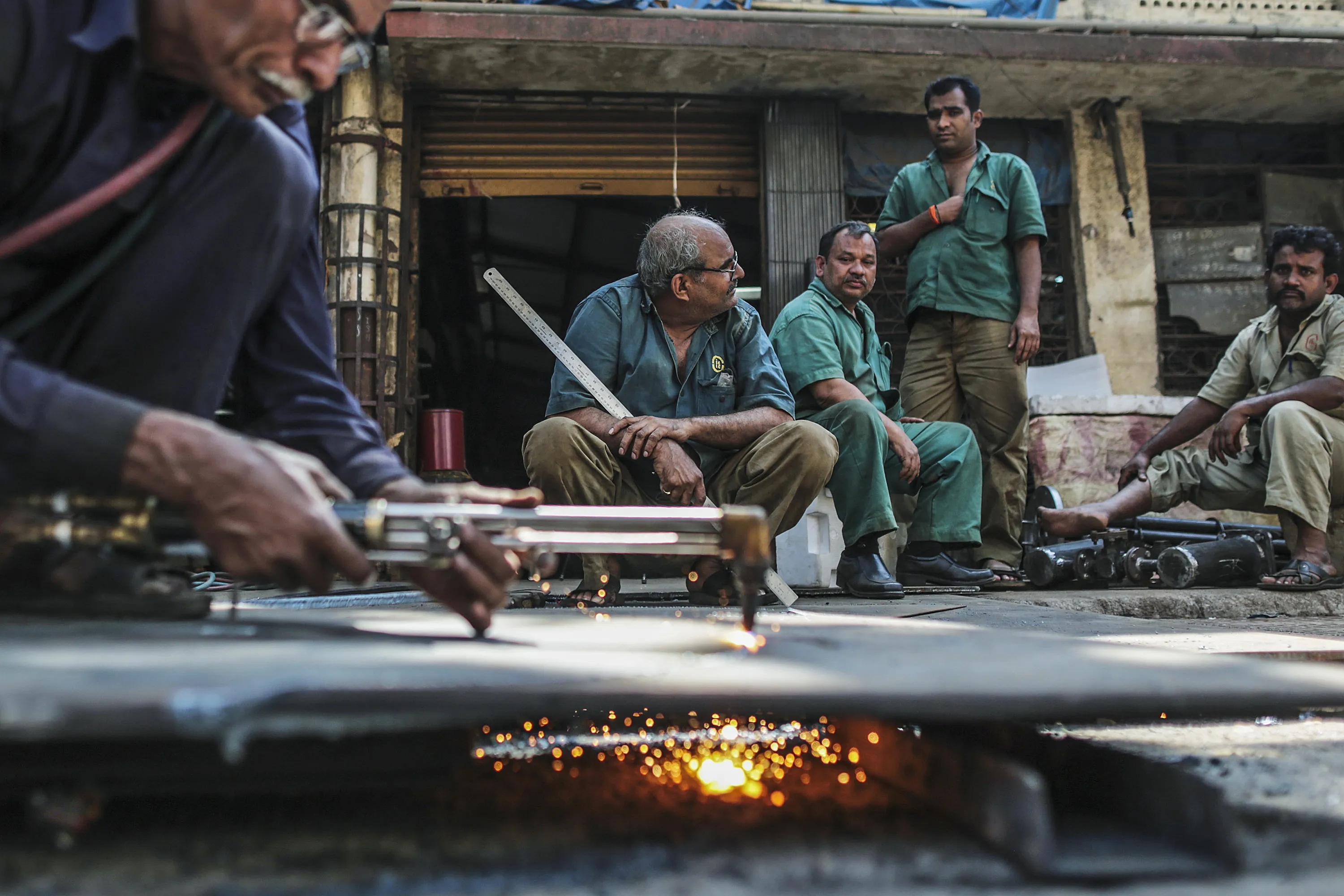 Employees sit round a colleague using a cutting torch at an Ishwar Engineering Co. factory in Mumbai, Maharashtra, India.
