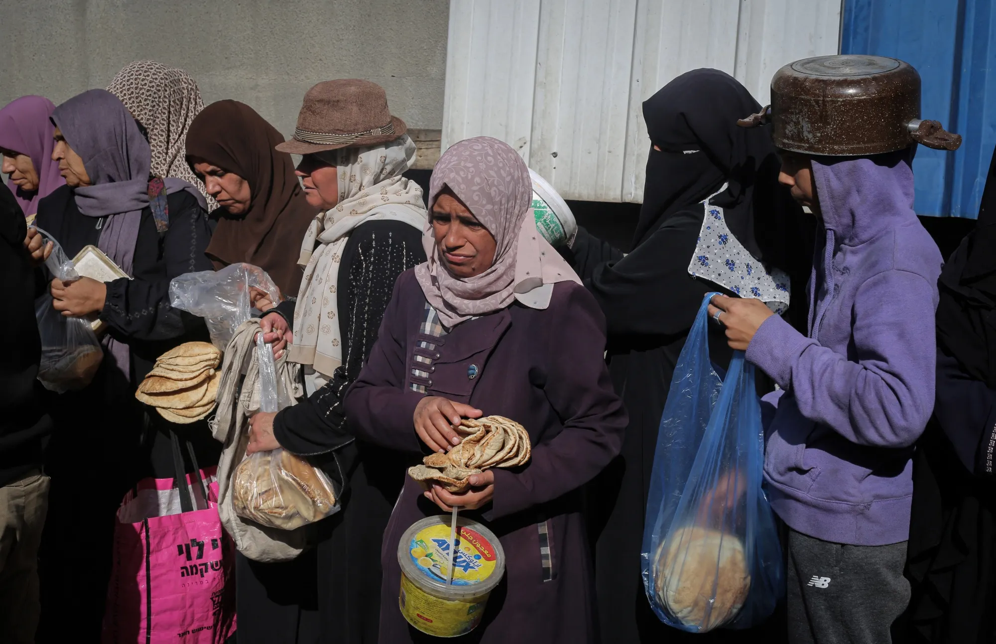 Displaced Palestinians, children and adults wait for a food portion at a shelter in Nuseirat, Gaza on Nov. 23.