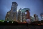 A pedestrian holding an umbrella walks past buildings illuminated at night in the Lujiazui district of Shanghai, China.