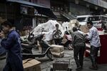A woman uses a smartphone, center, as workers move boxes at a street market in Chongqing.