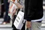 A woman uses a smartphone while carrying a bag displaying the SoftBank Group Corp. logo on a street in Tokyo, Japan, on Monday, Sept. 14, 2015. TT Docomo Inc. led declines among Japanese wireless carriers, plunging the most in almost seven years, after a report that Prime Minister Shinzo Abe said mobile phone rates should be reduced.