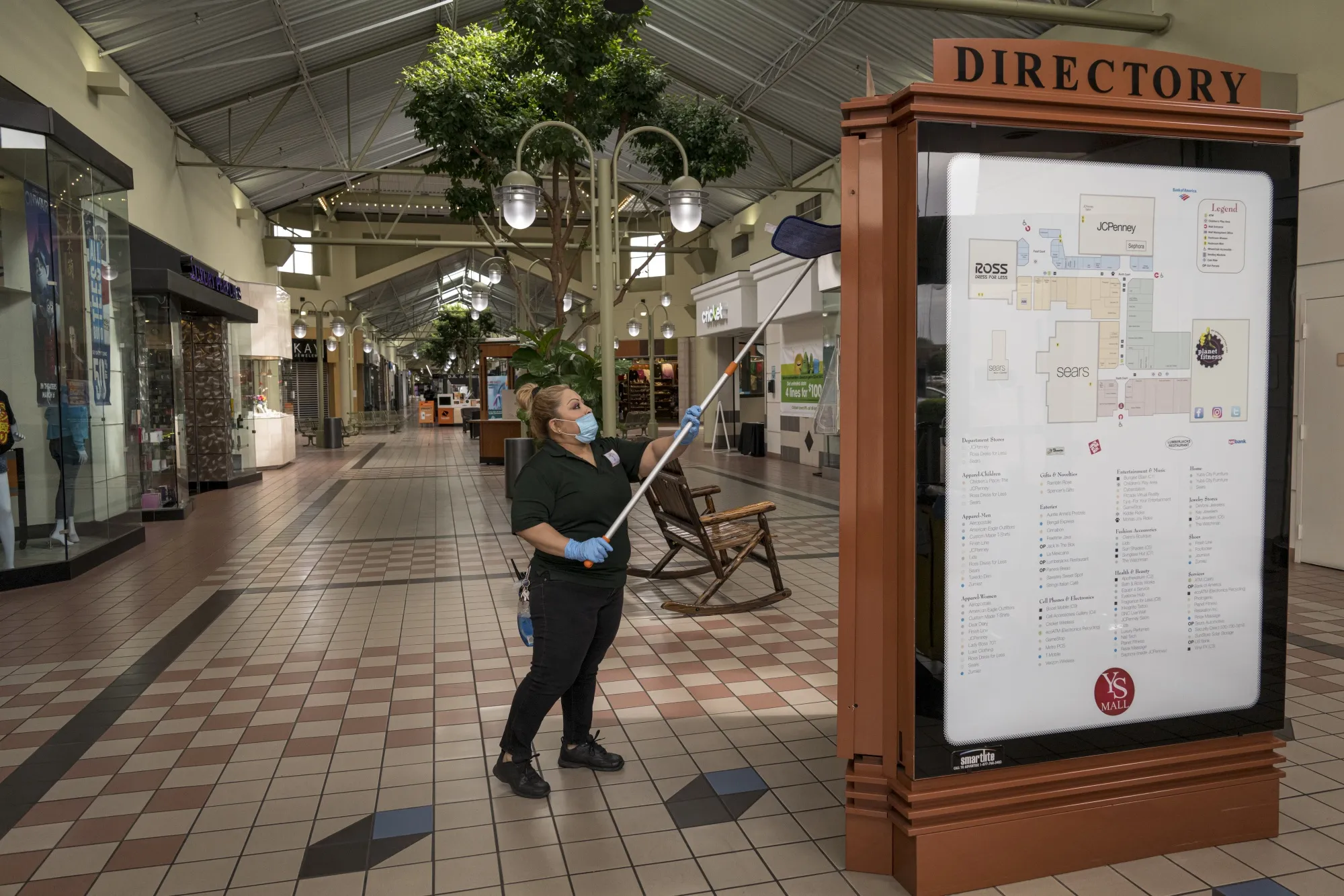 A worker wearing a protective mask and gloves cleans a directory at a mall in Yuba City, California on May 13.