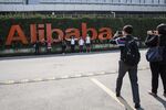 Visitors pose for photographs in front of a signage for Alibaba Group Holding Ltd. at the company's headquarters in Hangzhou, China, on Tuesday, Oct. 13, 2015. Alibaba's bet on data technology is driving greater investment in areas including ways to protect user privacy as it battles Amazon.com Inc. for customers globally.

