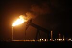 The silhouette of an electric oil pump jack is seen near a flare at night in Midland, Texas.