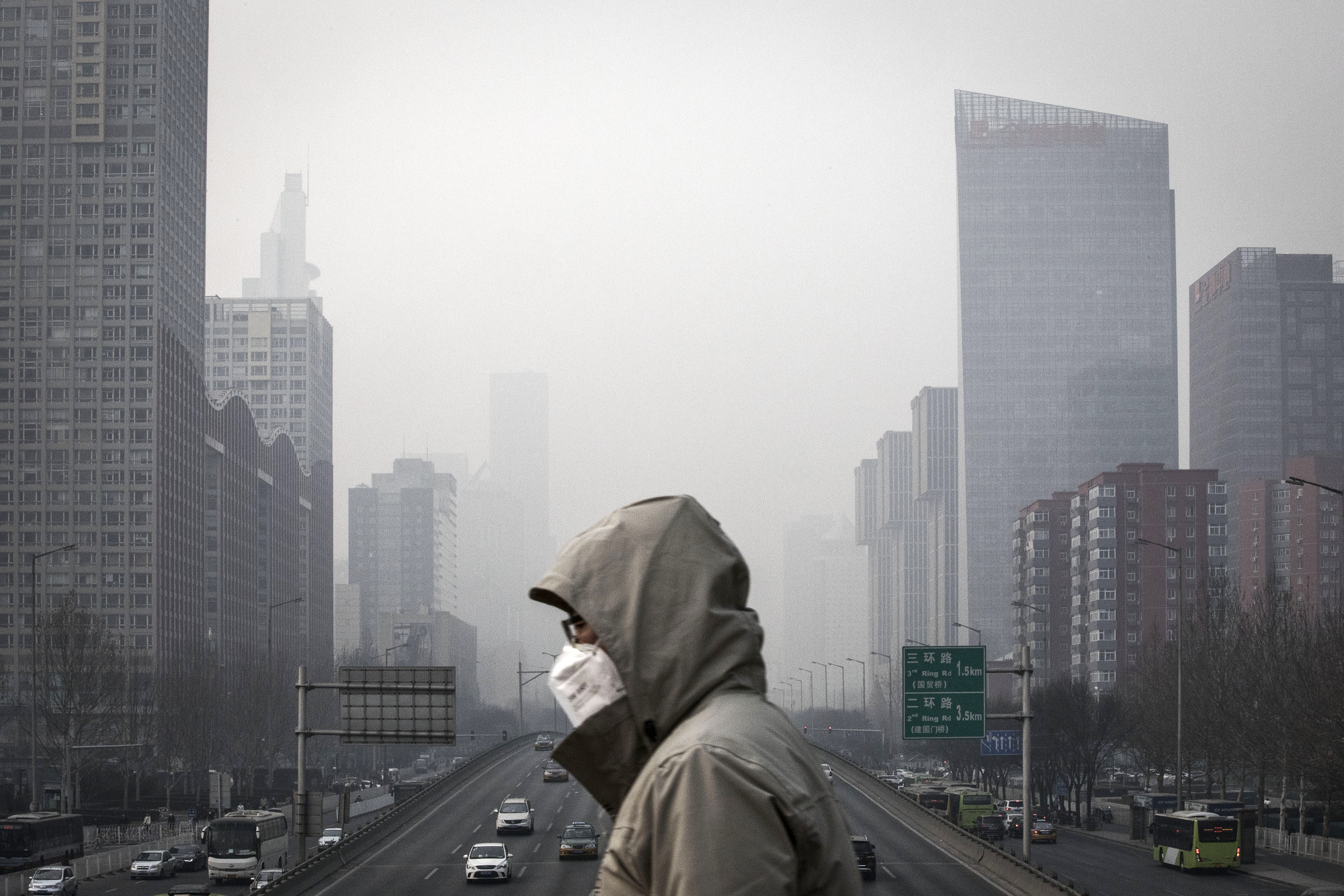 A man wearing a face mask walks on a footbridge as buildings shrouded in haze stand in Beijing.