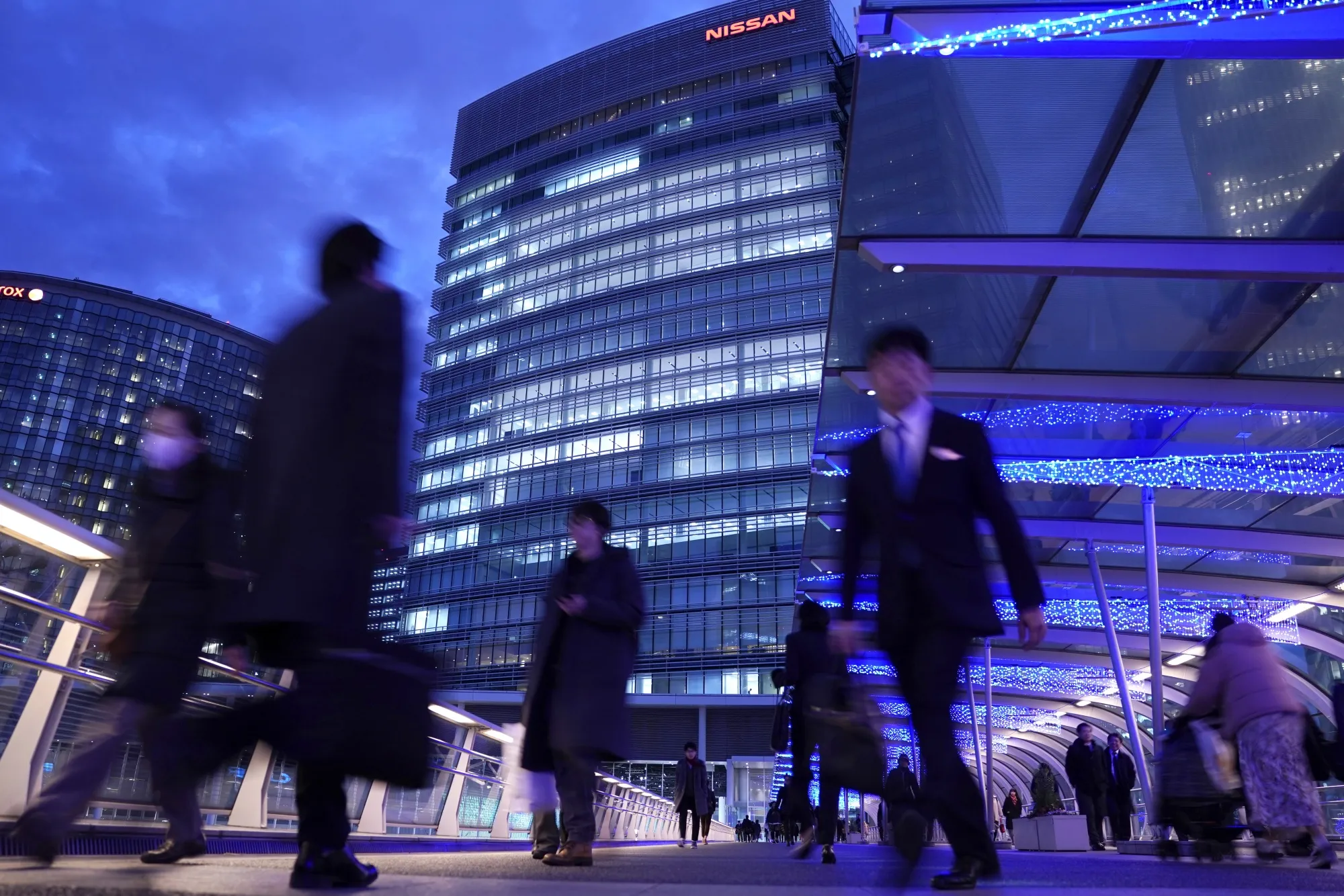 Pedestrians walk across a footbridge in front of the Nissan&nbsp;headquarters in Yokohama, Japan.