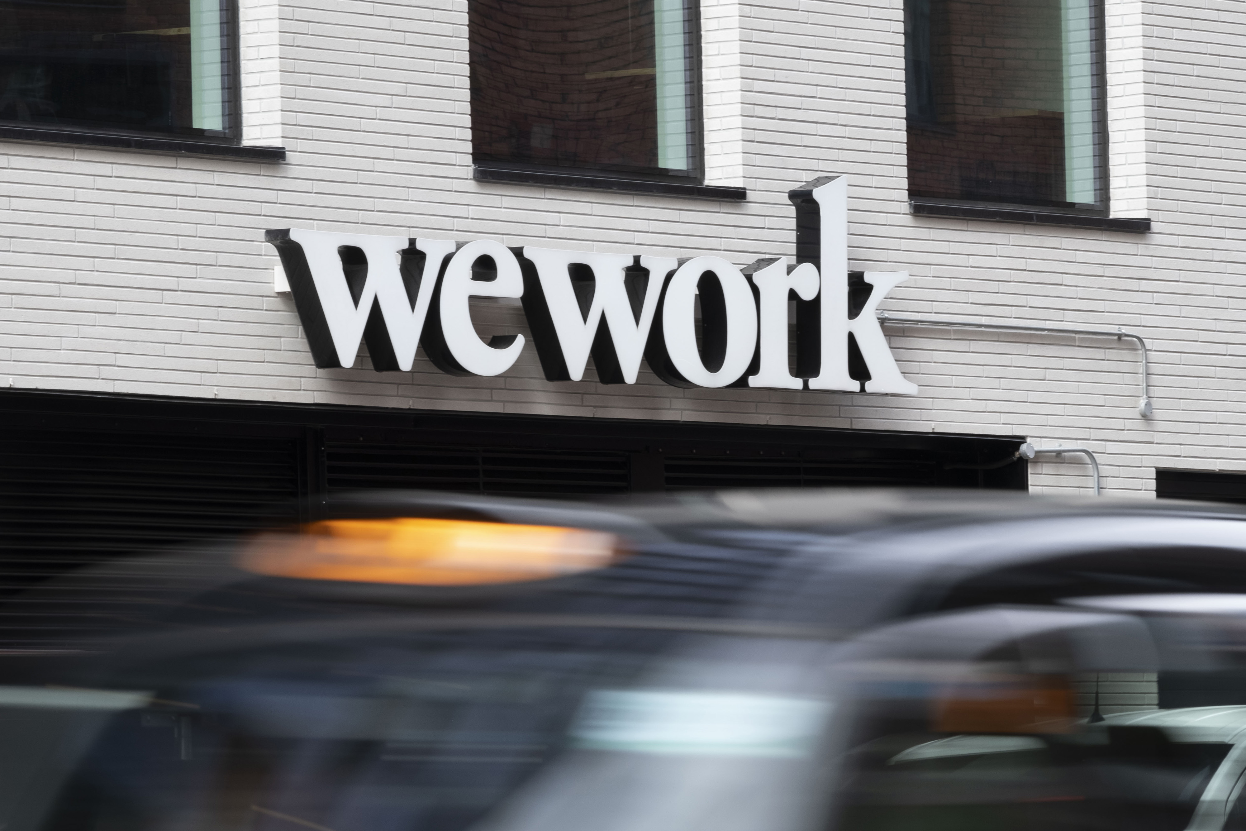A taxi drives past a logo for WeWork in London.