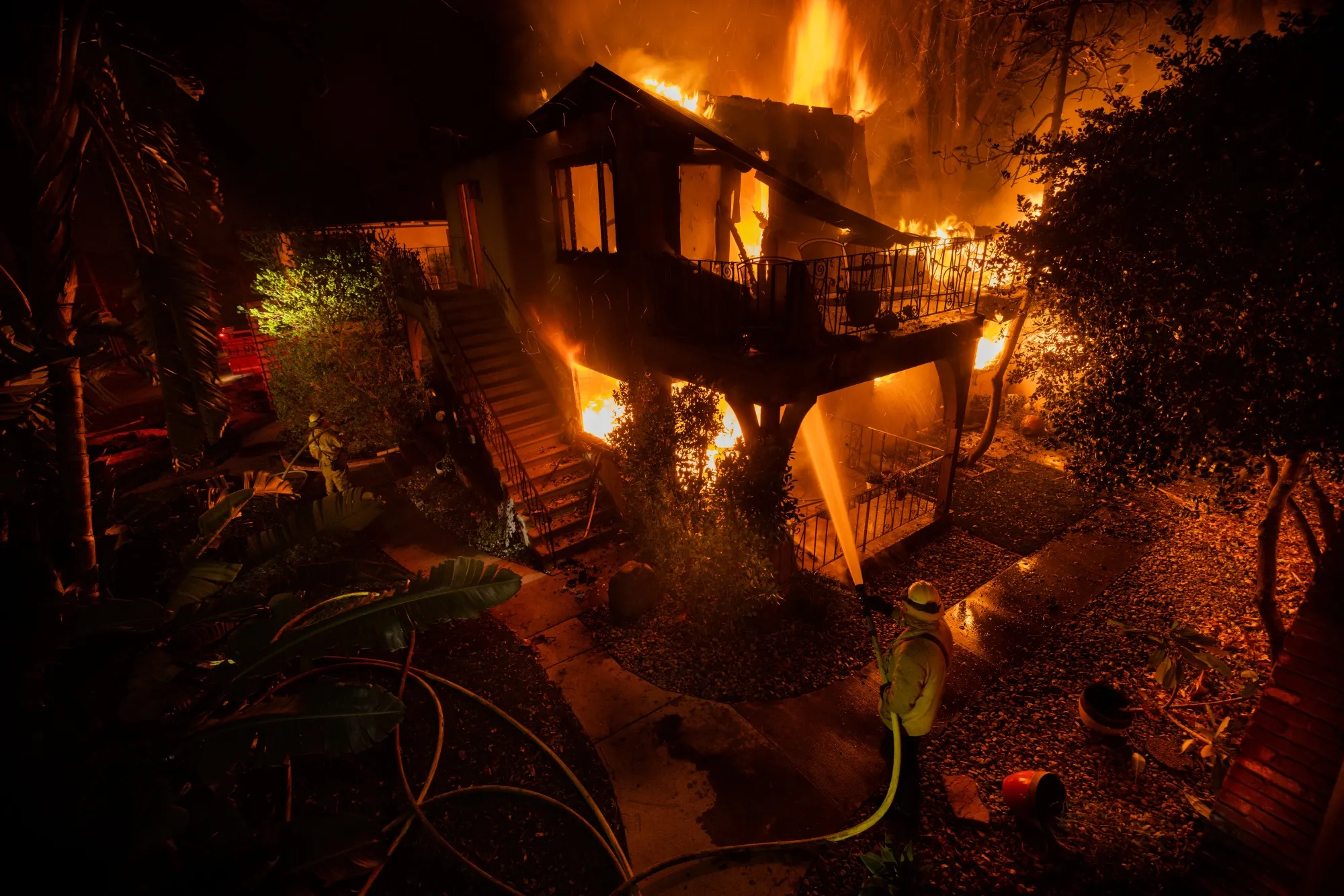 A firefighter hoses down a burning house.