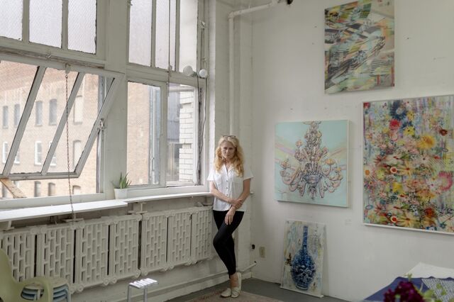 A portrait of Mary Ann Strandell in her studio next to her paintings. 