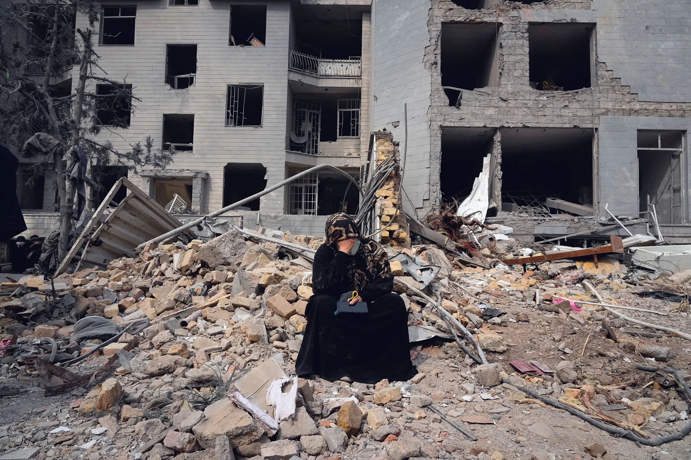 A woman sits amid rubble near a building damaged during an airstrike, in Tehran, on March 12.