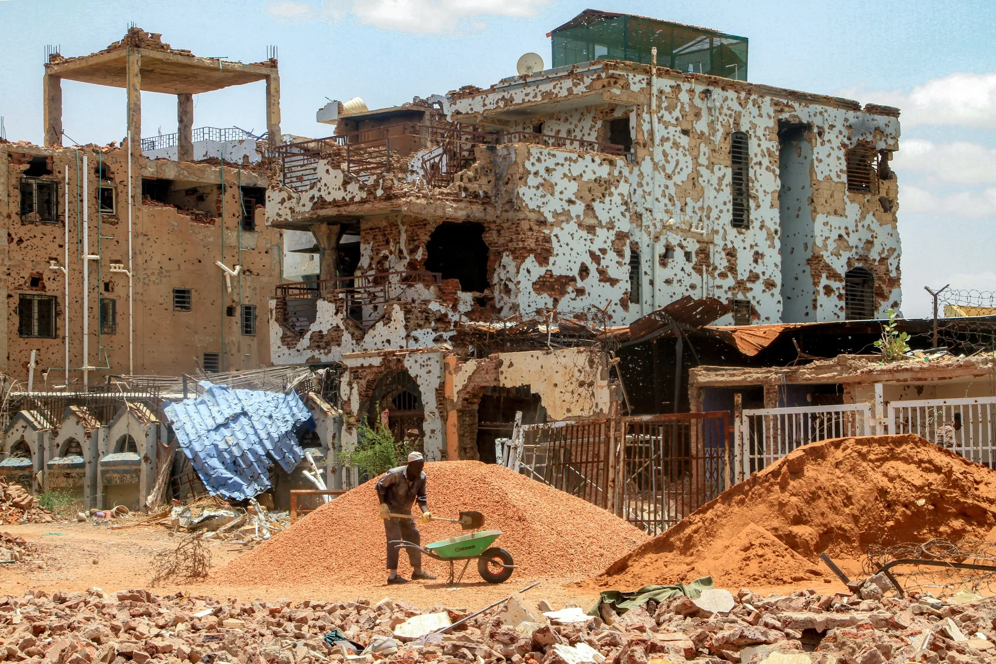 A worker shovels pebbles near&nbsp;heavily-damaged buildings in Khartoum on July 30.