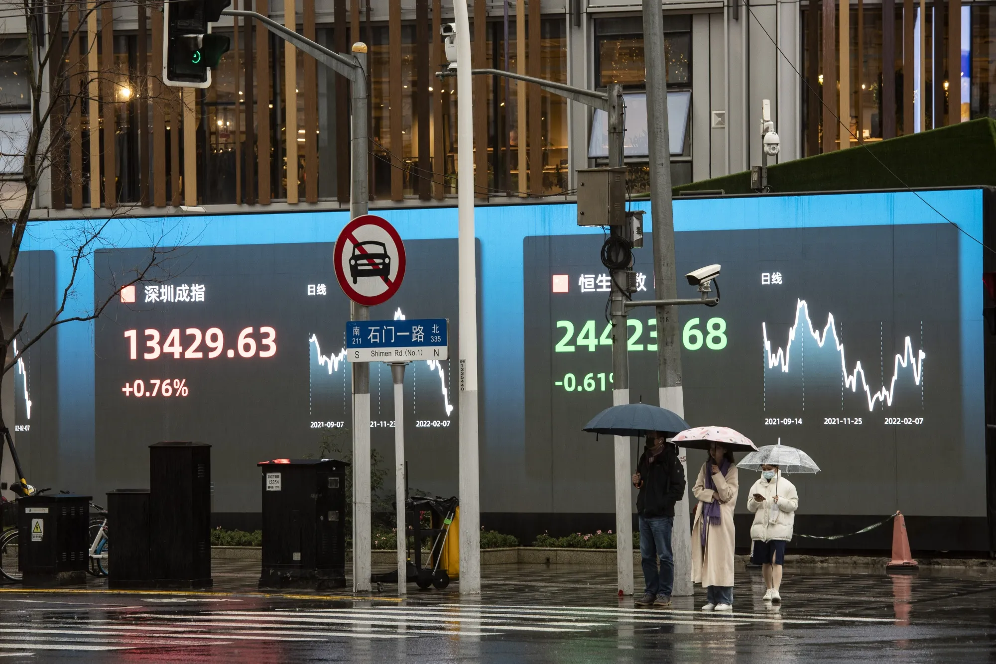 Pedestrians wait to cross a road in front of a screen displaying the Shenzhen Stock Exchange and the Hang Seng Index figures in Shanghai, China, on&nbsp; Feb. 7.