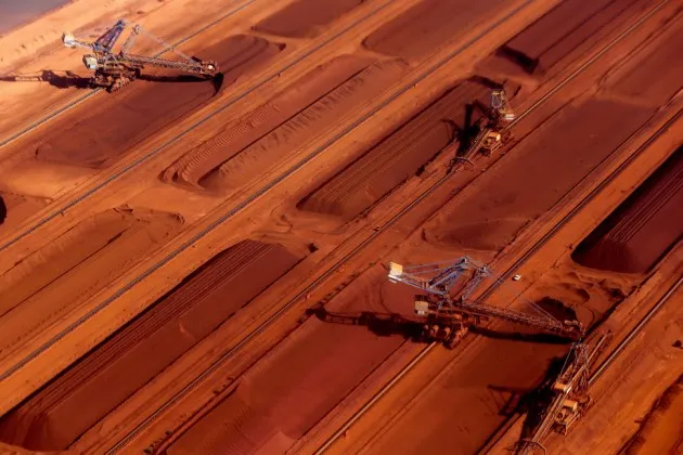 Stackers operate next to stockpiles of iron ore at a processing facility in the Pilbara region of western Australia