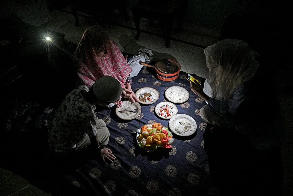A family eats dinner at home by the light of a mobile phone&nbsp;during a power cut in Islamabad, on April 15.