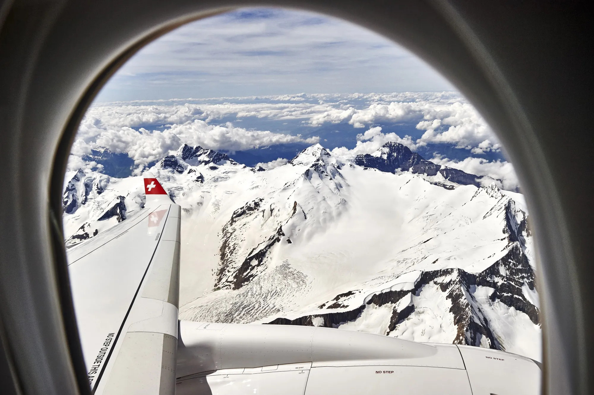 The Swiss Alps are seen through an aircraft window.