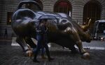 Pedestrians carry an umbrella while walking past the Charging Bull sculpture in New York.