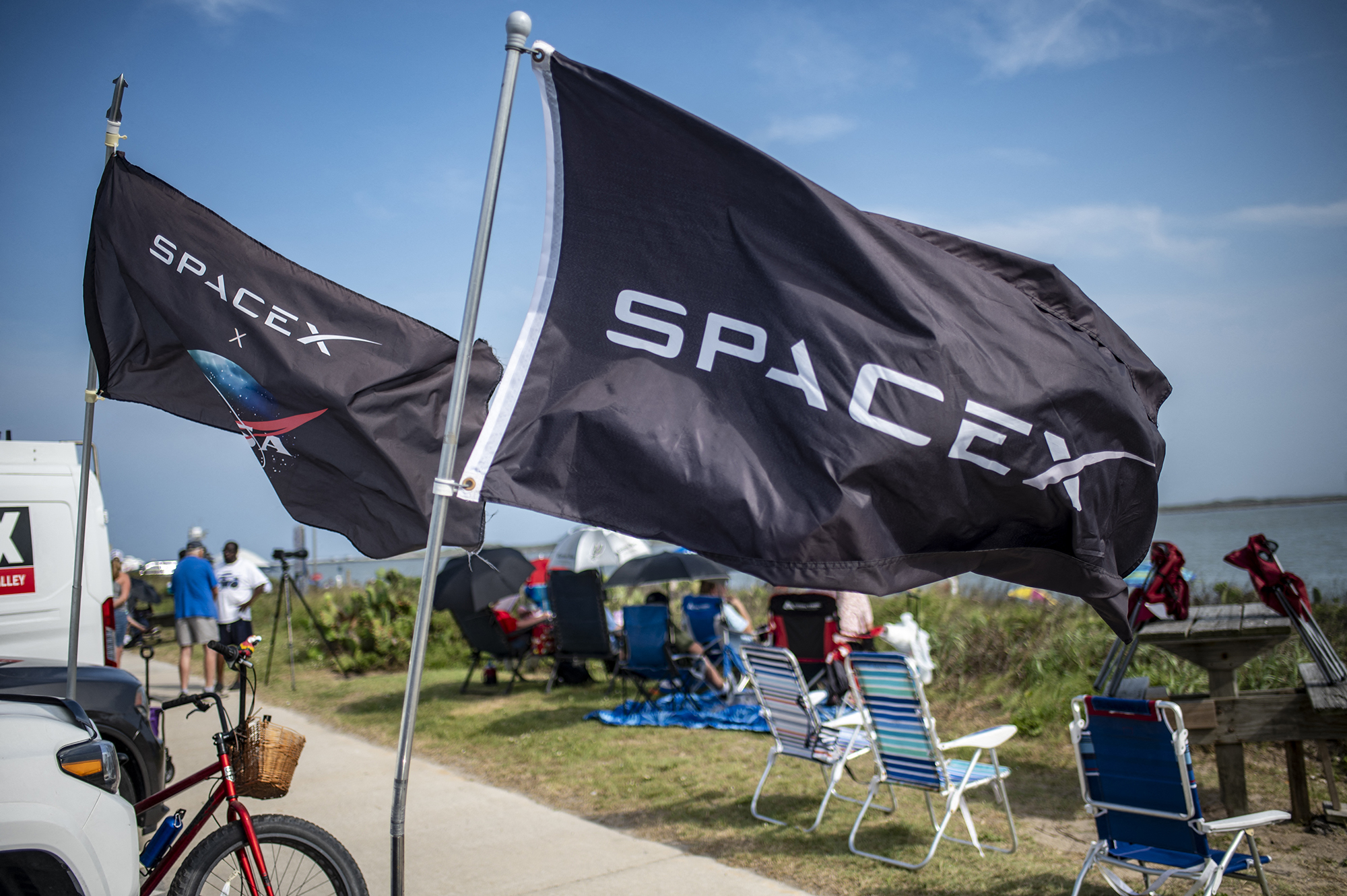 SpaceX flags fly as people wait on South Padre Island to watch a SpaceX Starship rocket launch from Starbase, Texas. Photographer: Sergio Flores/AFP/Getty Images