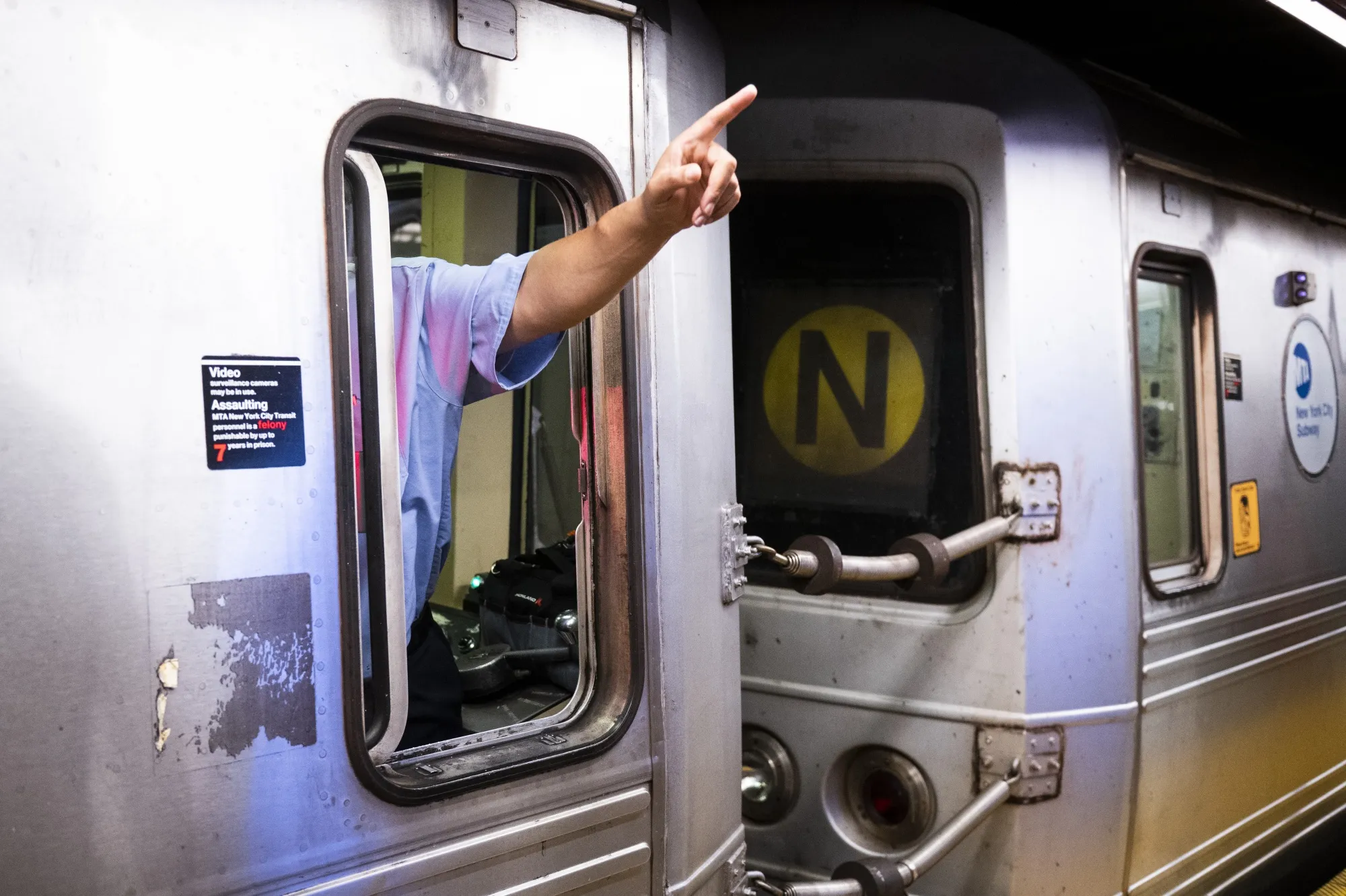A conductor in a train points to a sign at a subway station in New York.