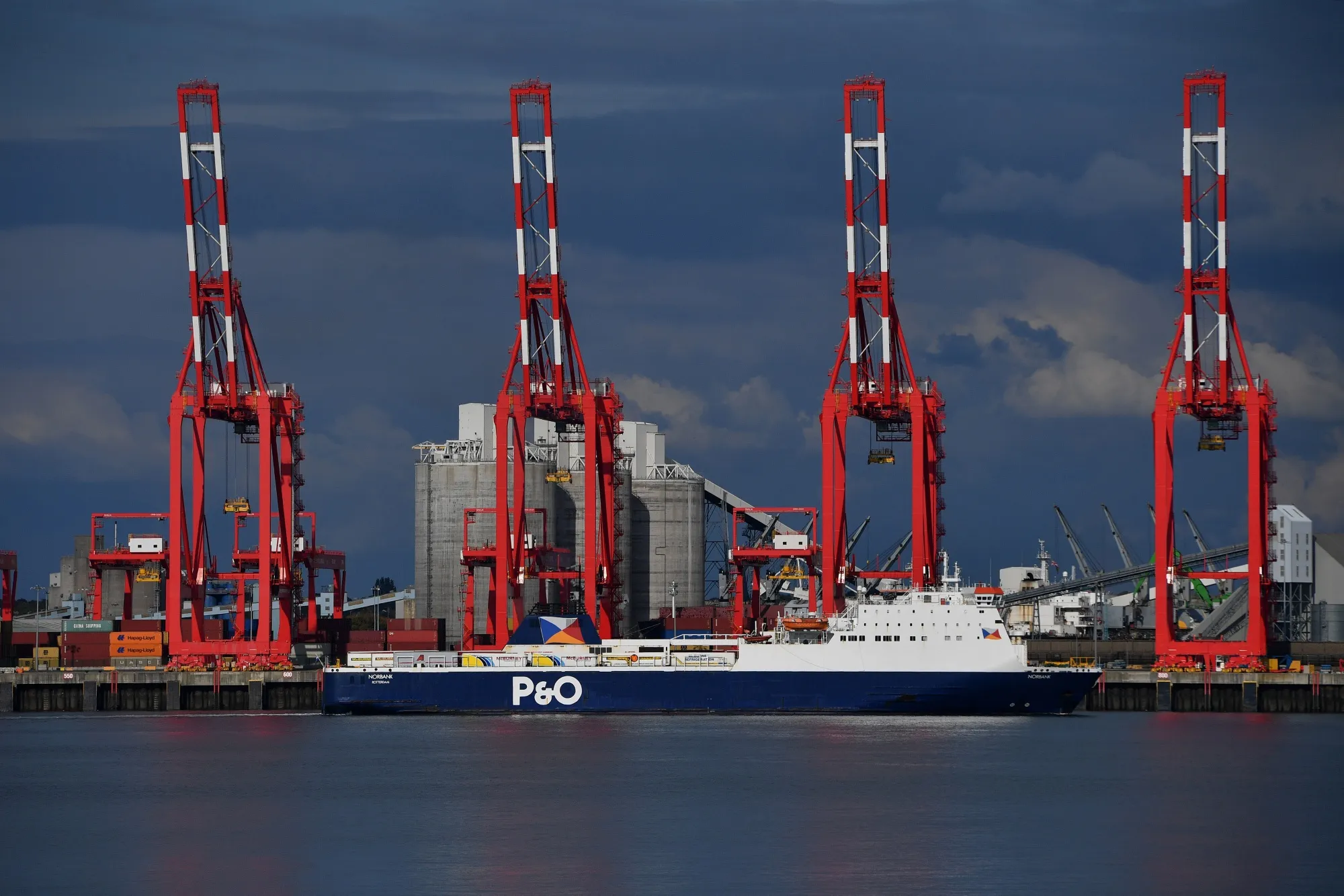 A freight vessel sails past ship to shore cranes at the Port of Liverpool in Liverpool, UK.