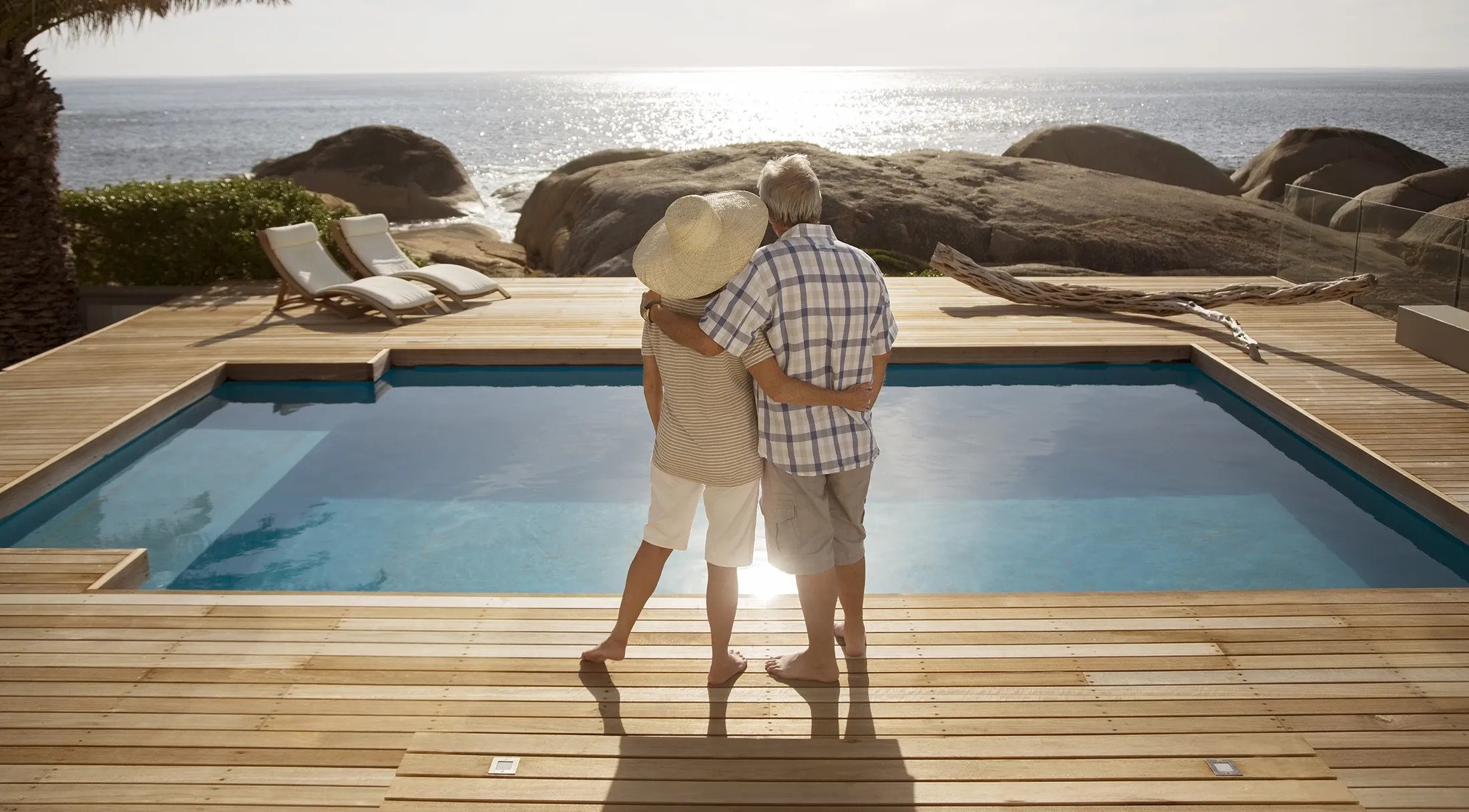Senior couple hugging by modern pool overlooking ocean