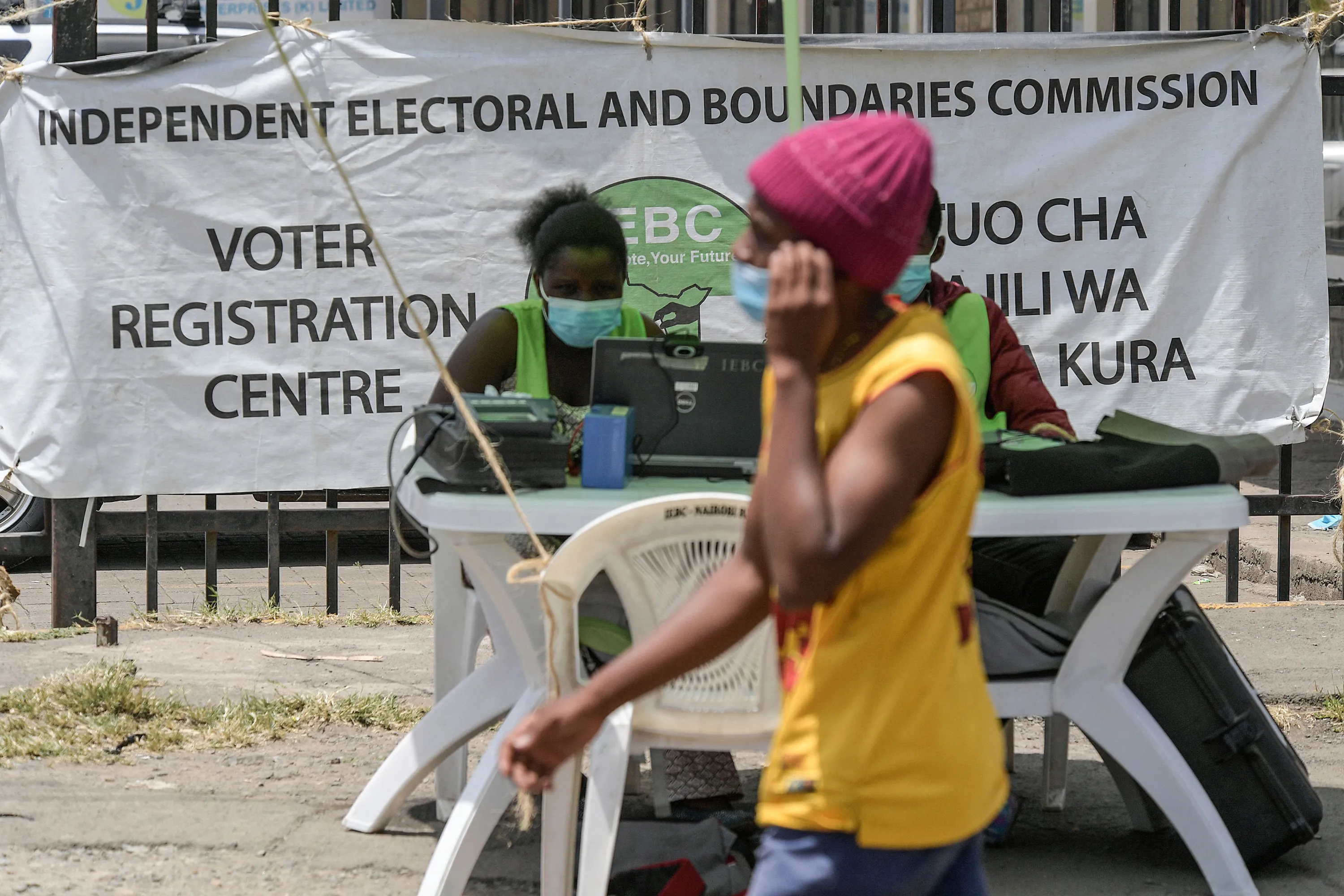 A man passes workers for the Independent Electoral and Boundaries Commission&nbsp;in Nairobi,&nbsp;during the voters registration campaign ahead of the 2022 Kenyan general election, in Nairobi, Kenya, on Feb. 4.&nbsp;