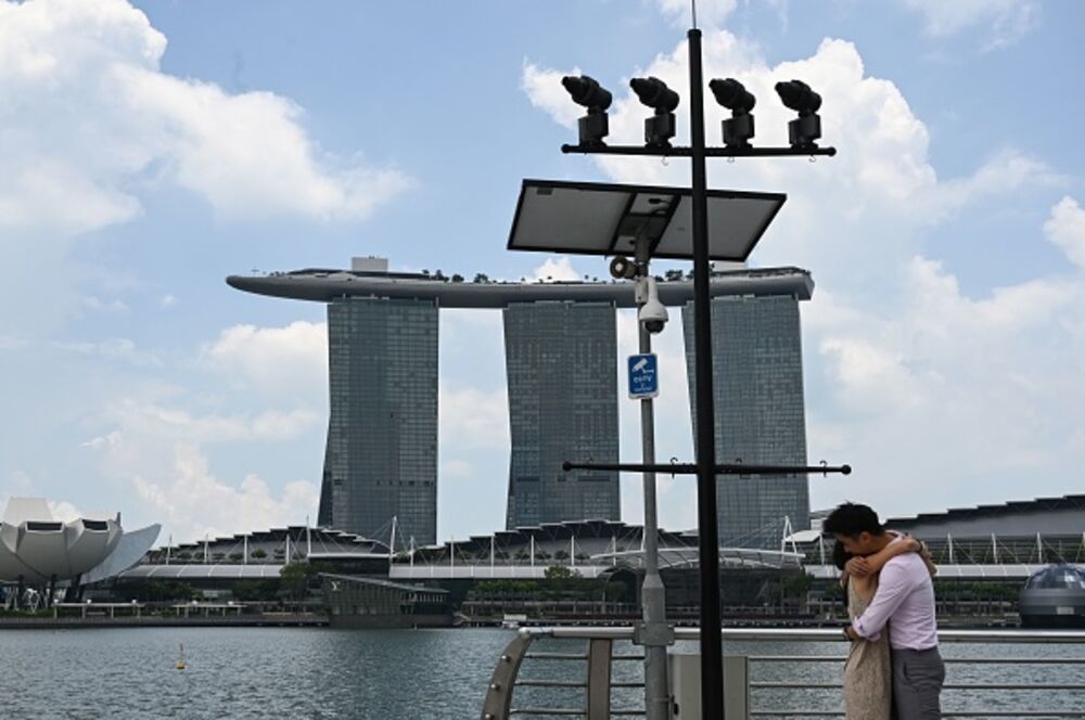 A couple hugs under a closed circuit television (CCTV) surveillance camera in Marina Bay in Singapore on April 2, 2020, as the government slowly tightens restrictions to combat the spread of the COVID-19 novel coronavirus.