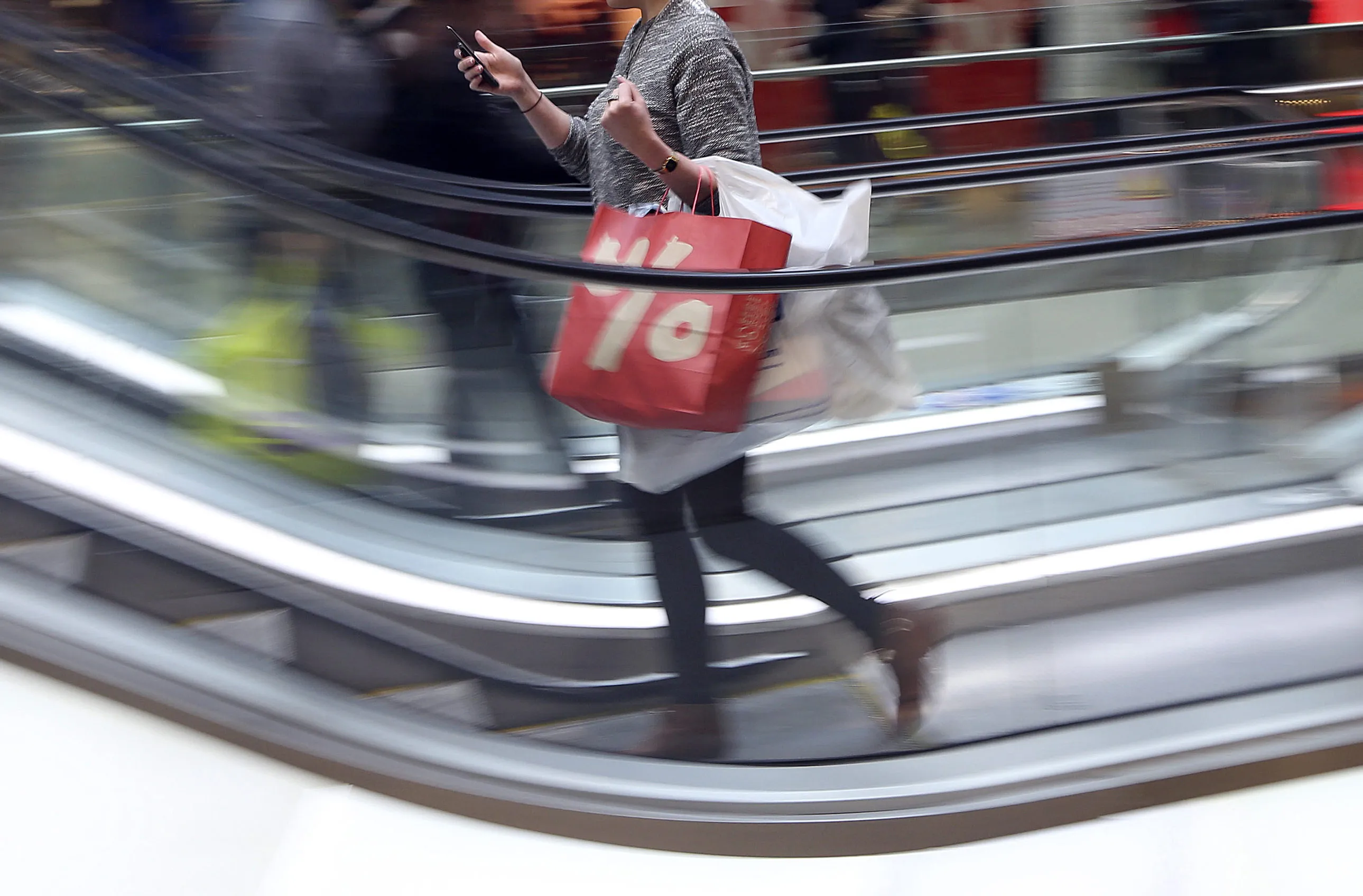 A pedestrian uses her mobile phone whilst carrying branded shopping bags inside the Westfield Stratford City shopping mall in London, U.K., on Thursday, Dec. 27, 2012. Overall Christmas shopping in the U.K. was similar to last year, according to the British Retail Consortium.
