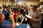 Job seekers line-up to give their resumes to an employment agency representivie at a job fair at a Holiday Inn in New York City.