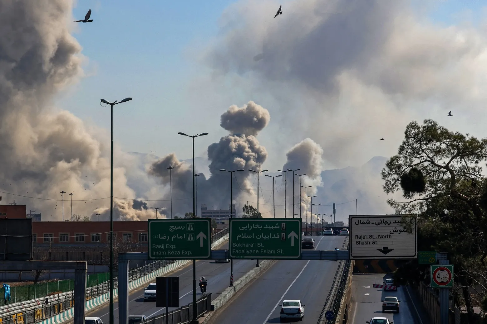 Motorists drive along an expressway as plumes of smoke rise after a strike in Tehran on March 5.