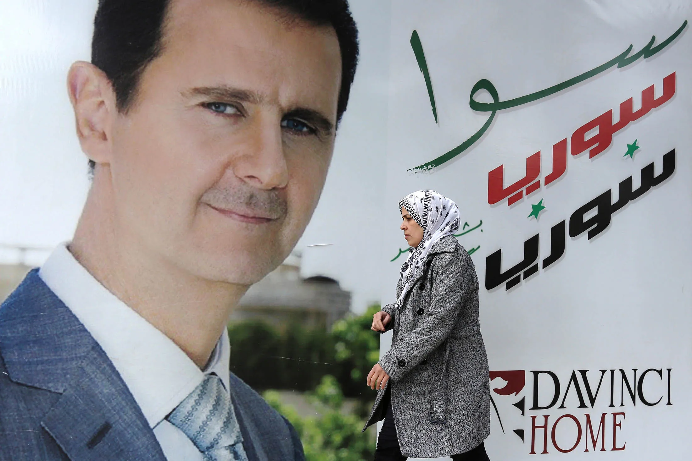 A Syrian woman walks past a placard bearing a portrait of President Bashar al-Assad.

