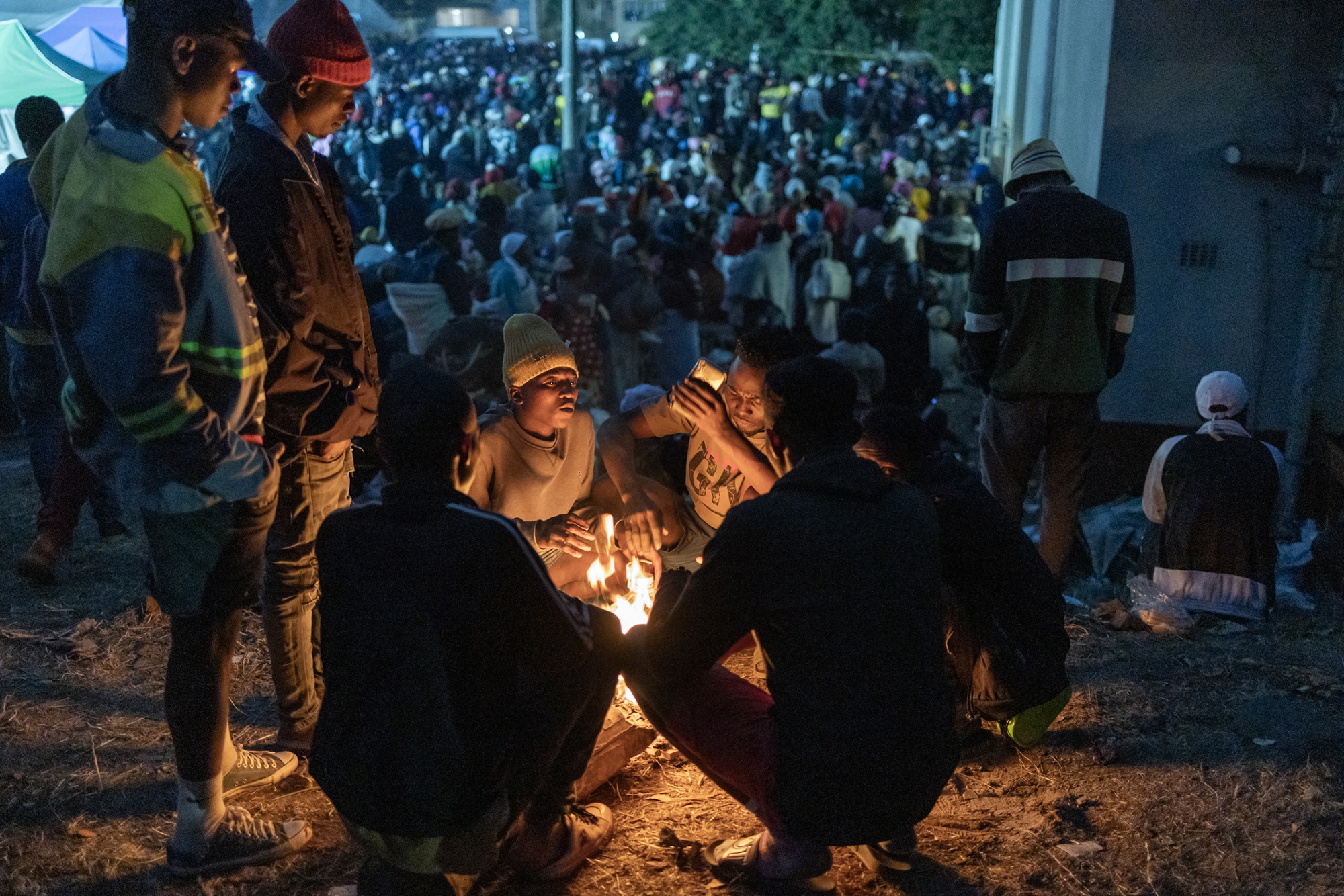 TOPSHOT - As the sun sets a few foreign nationals light a fire to keep warm from the winter cold at the Sherwood Park in Durban on June 13, 2026 as more than 7,000 people, mostly Malawian nationals, await another night before repatriation to Malawi. The situation reflects growing tensions fuelled by public frustration over chronic unemployment and slow economic growth. South Africa is home to millions of foreign nationals, many of whom have migrated from other African countries in search of better opportunities. Hundreds of migrants await repatriation to Malawi from South Africa following xenophobic violence in the country. (Photo by Rajesh JANTILAL / AFP via Getty Images) Photographer: RAJESH JANTILAL/AFP