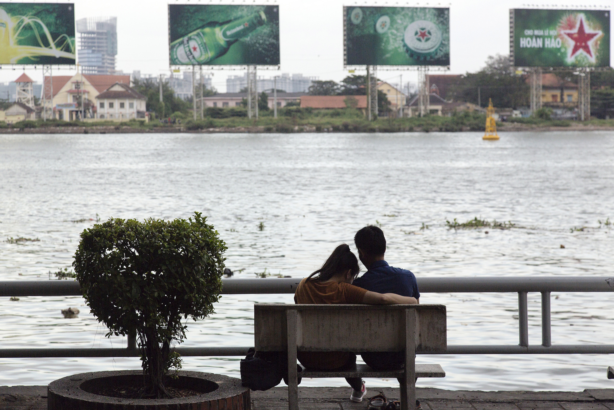 A couple sits on a bench on the banks of a river in Ho Chi Minh City, Vietnam.