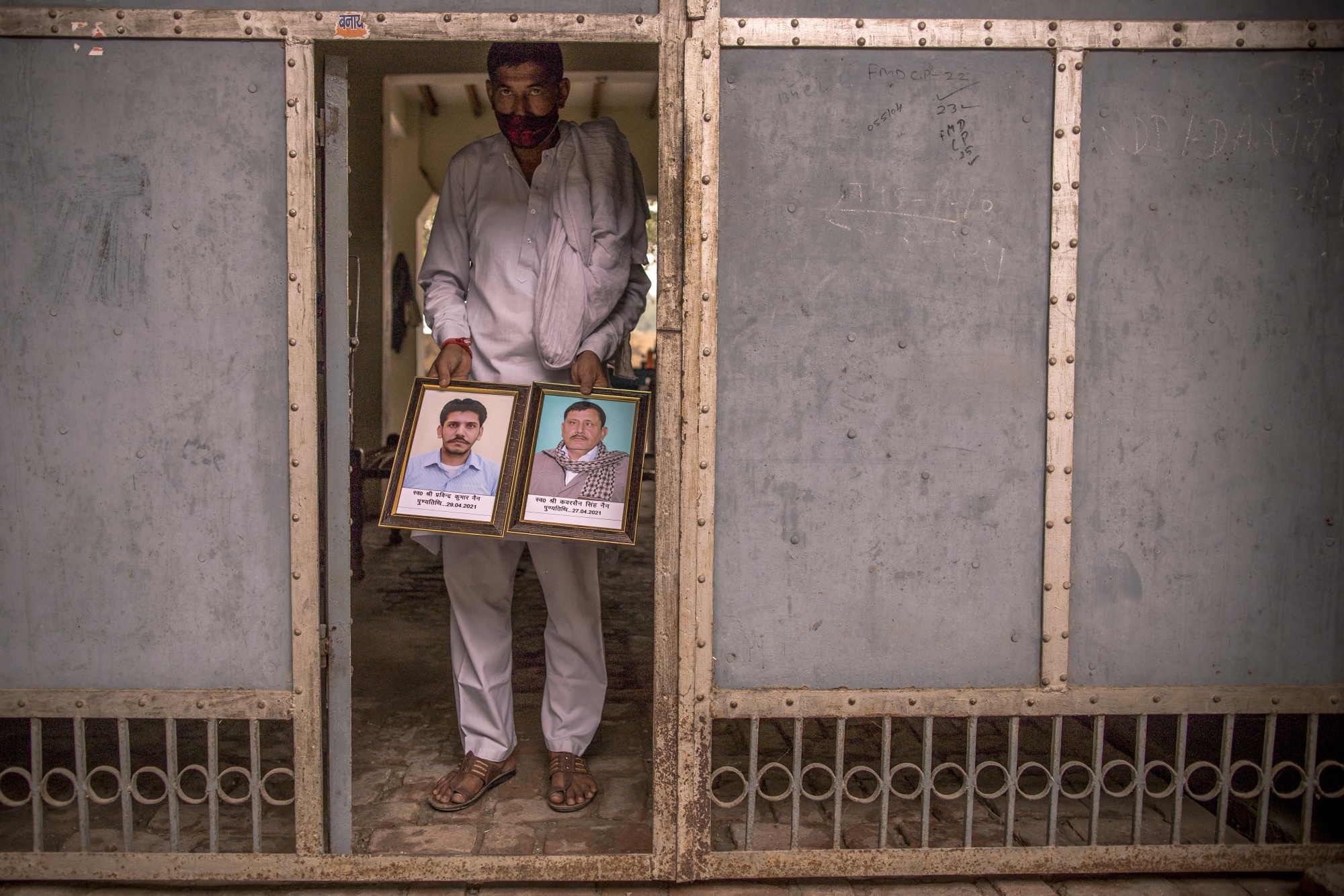 Village Pradhan / Head brings out the portrait of Covid fatalities Kuwarsen Singh (R) and his son Pravinder Kumar. Kuwarsen singh was sent to an election duty where he was infected with the Covid virus. Picture taken at his house in the village Bassi, in Baghpath, Uttar Pradesh, India