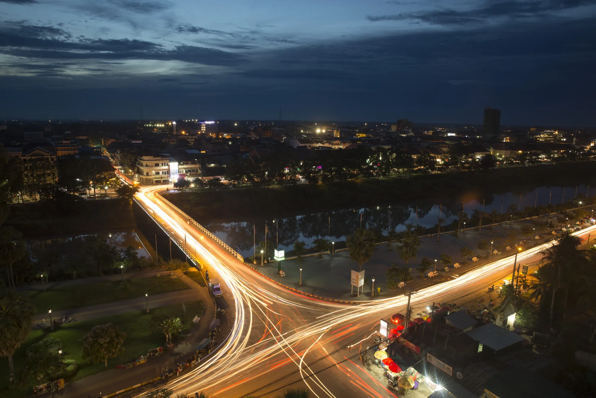Light trails from moving traffic run along a road and bridge at night in Battambang, Cambodia.