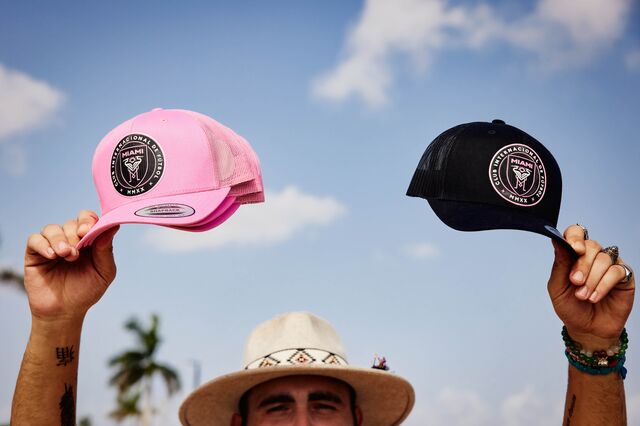 A man holds up three pink and three black Inter Miami hats for sale.