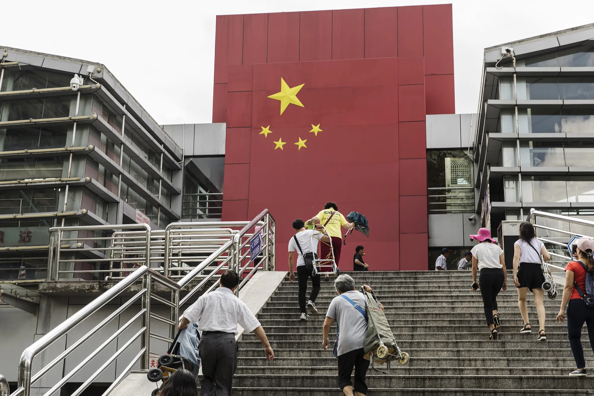 People walk up a flight of stairs as a Chinese flag is displayed at a border crossing facility in the Sha Tou Jiao Port of Shenzhen.