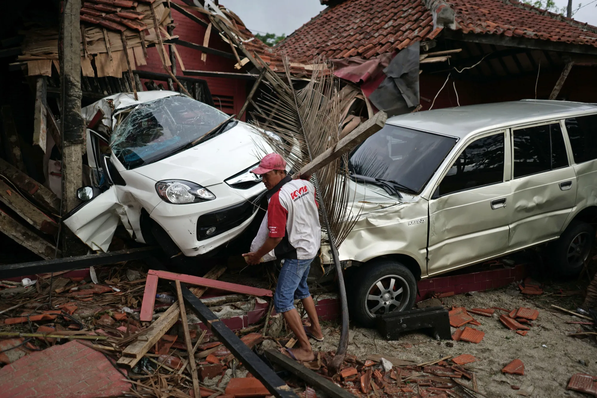 A man clears debris in front of damaged cars and buildings at the Villa Avi Redita in Carita, Banten province, Indonesia, on&nbsp;Dec. 24, 2018.