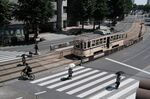 Pedestrians and a cyclist cross a street passing a tram in Kumamoto, Japan.