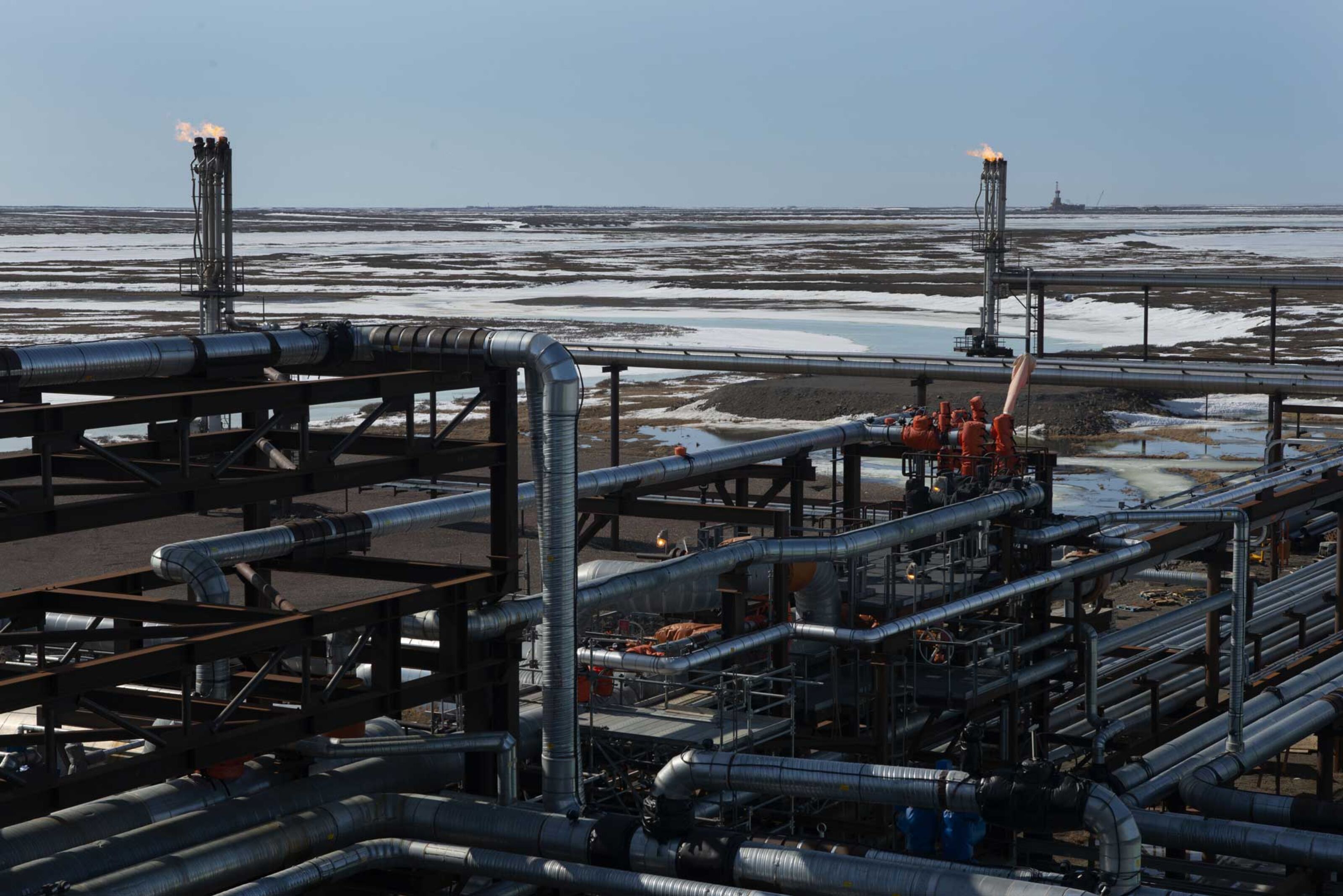 A network of pipes form a section of the processing facility at Conoco’s Alpine oil field on the North Slope, with a drill rig seen in the distance, across the tundra.