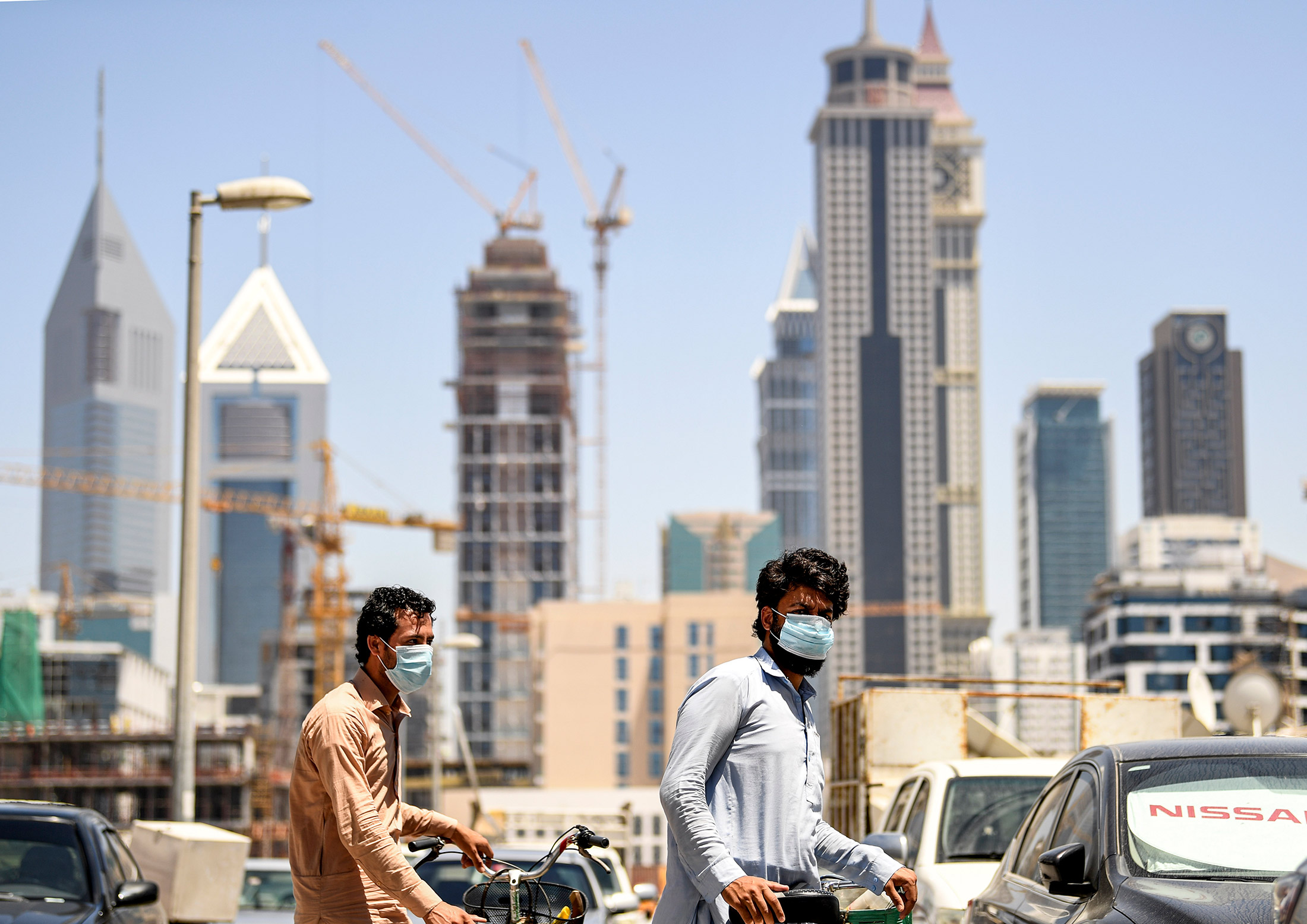 People wearing protective masks push&nbsp;bicycles along a street in the Satwa district of Dubai on May 6.&nbsp;