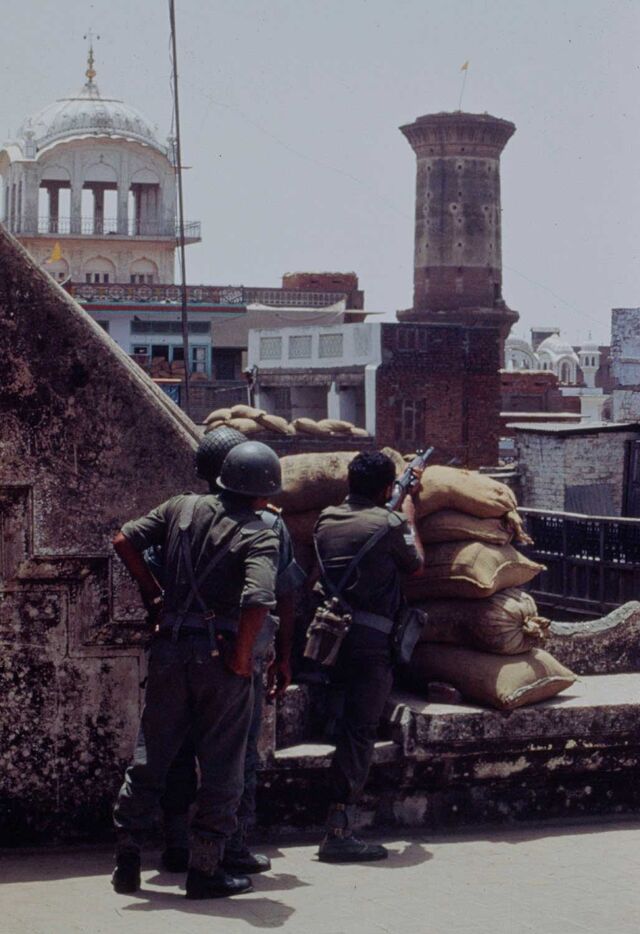 Archival photograph showing the backs of three soldiers barricaded on a building rooftop. One has a rifle that's pointed away from the building