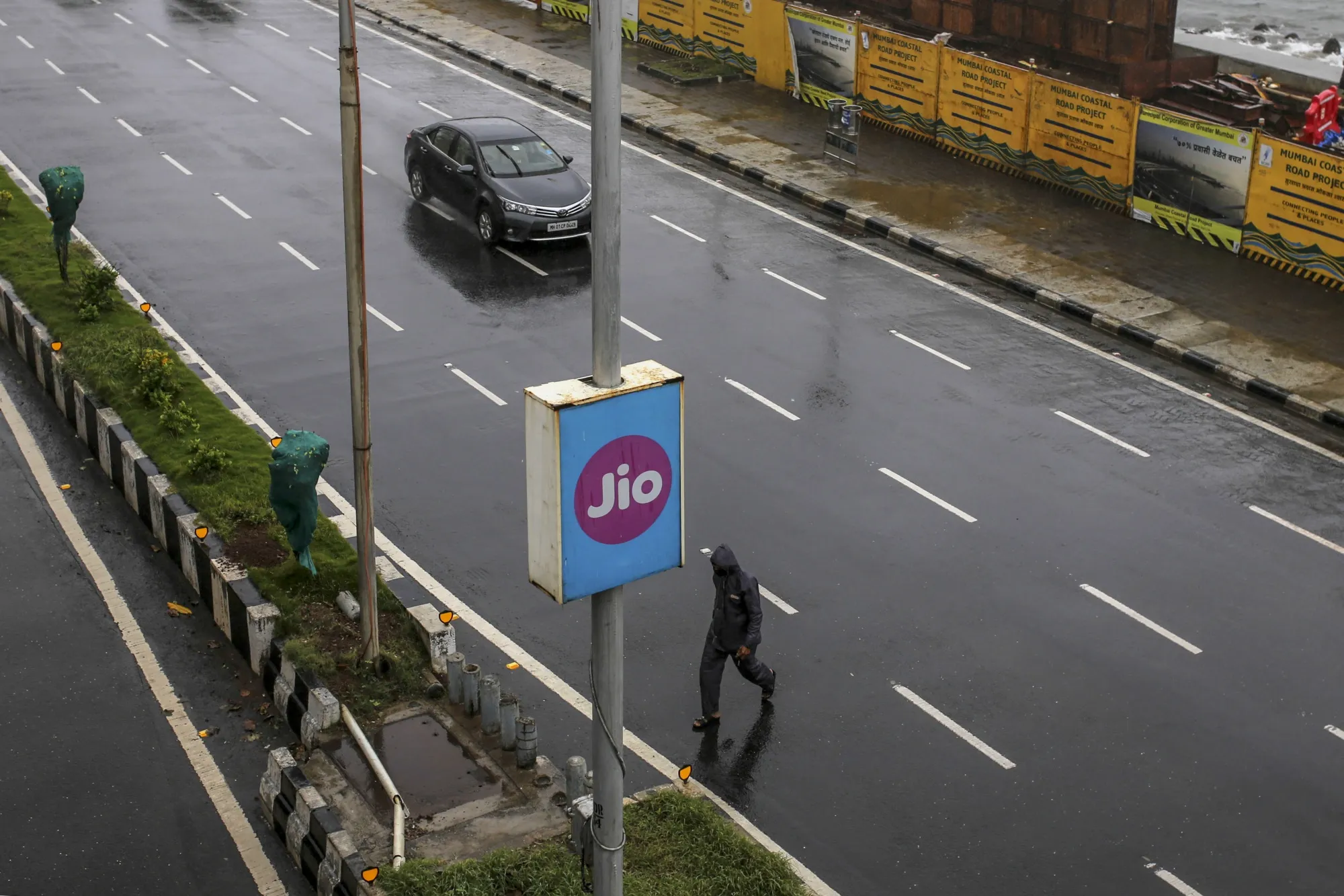 A pedestrian crosses a road as an advertisement for Jio Platforms Ltd. is displayed at Marine Drive in Mumbai.
