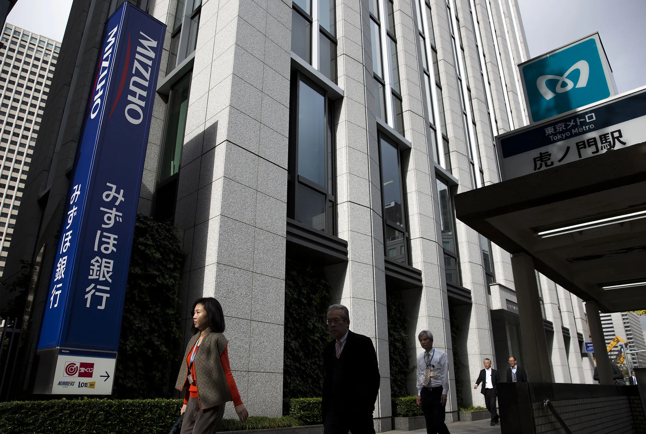 Pedestrians walk past a Mizuho Bank Ltd. branch in Tokyo.