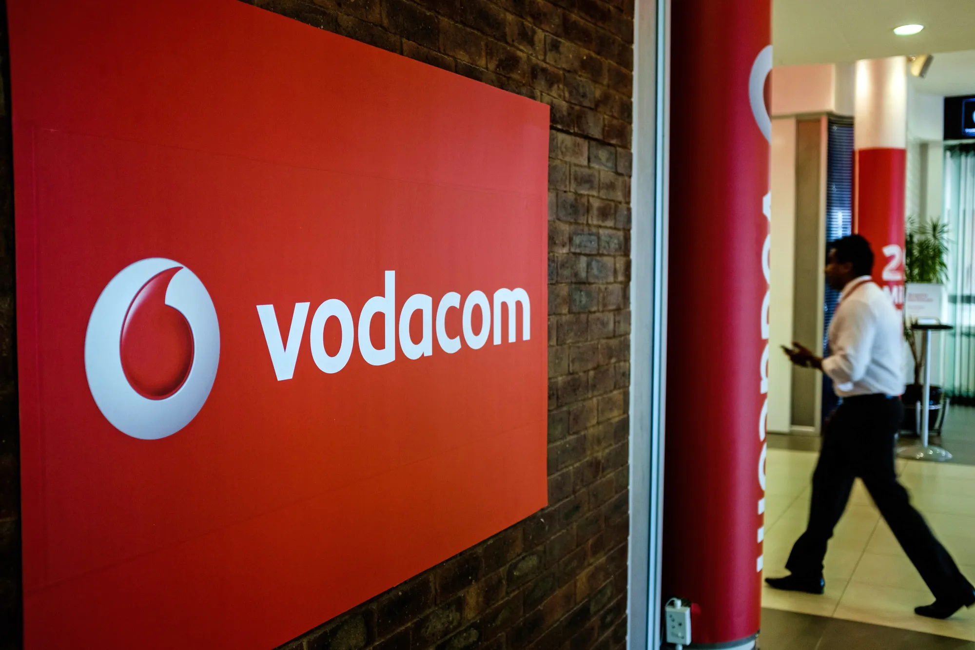 An employee passes a Vodacom Group Ltd. logo.