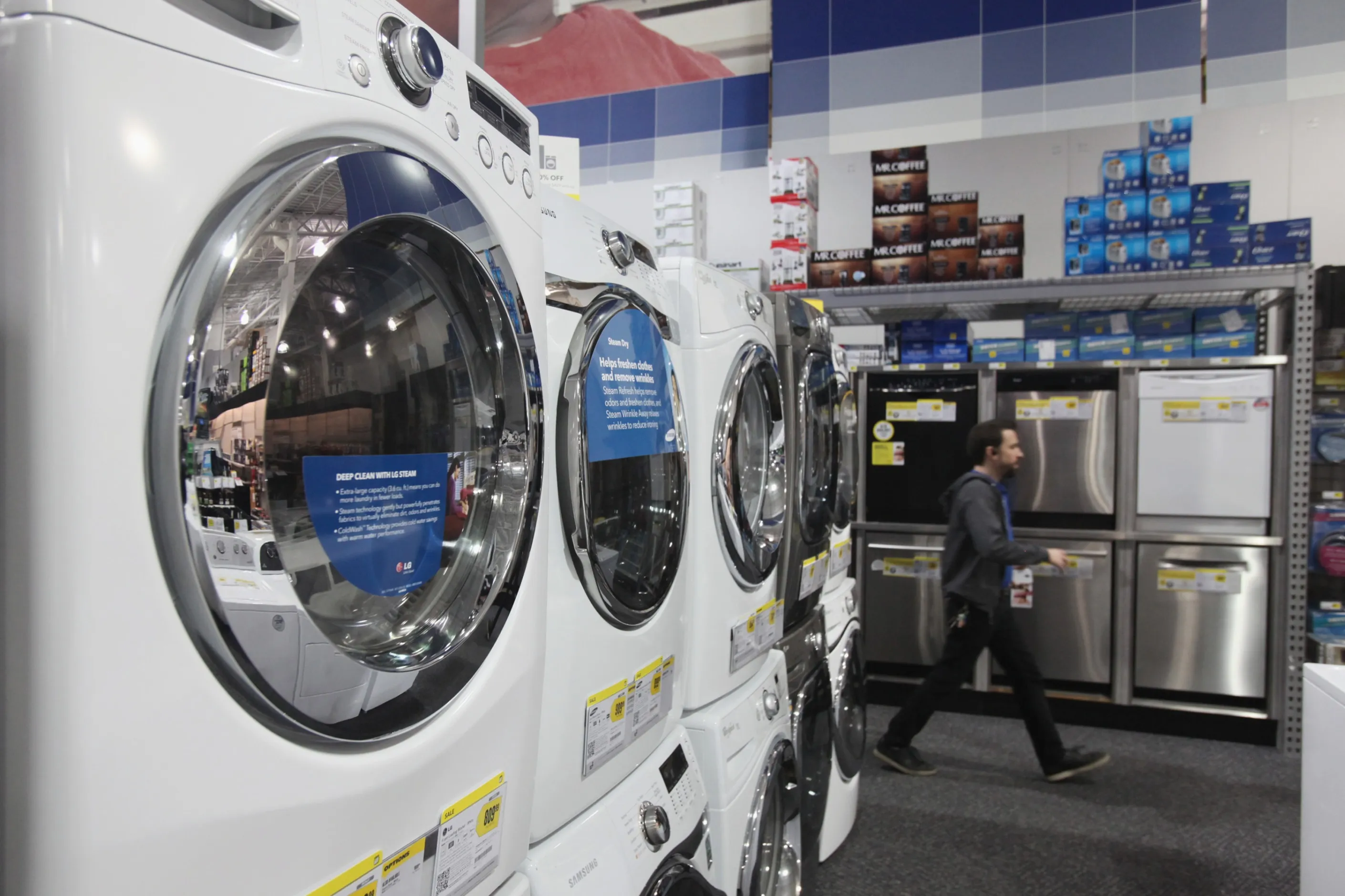 A man walks past appliances including washers and dryers for sale.