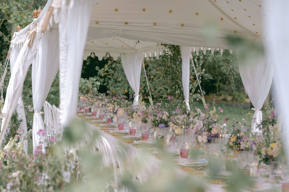 A marquee set up for a wedding breakfast. A long table is laid with china, pink glasses and vases filled with English country flowers.