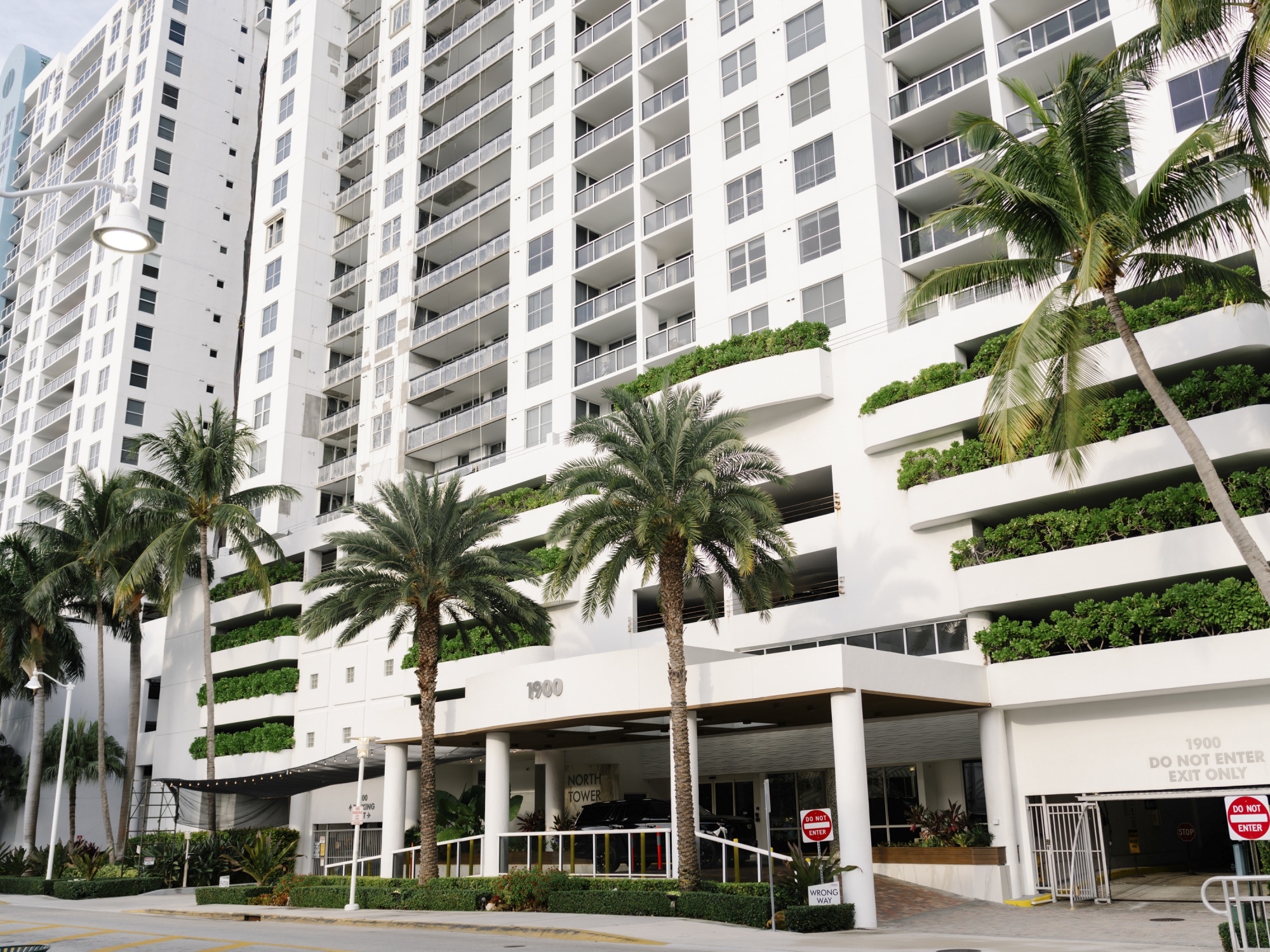 An image of a white condo in Miami Beach, palm trees are on the ground level.