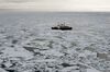A large boat sits in the middle of open water. The light reflecting off the mosaic of broken ice surrounding the boat is the palest orange.