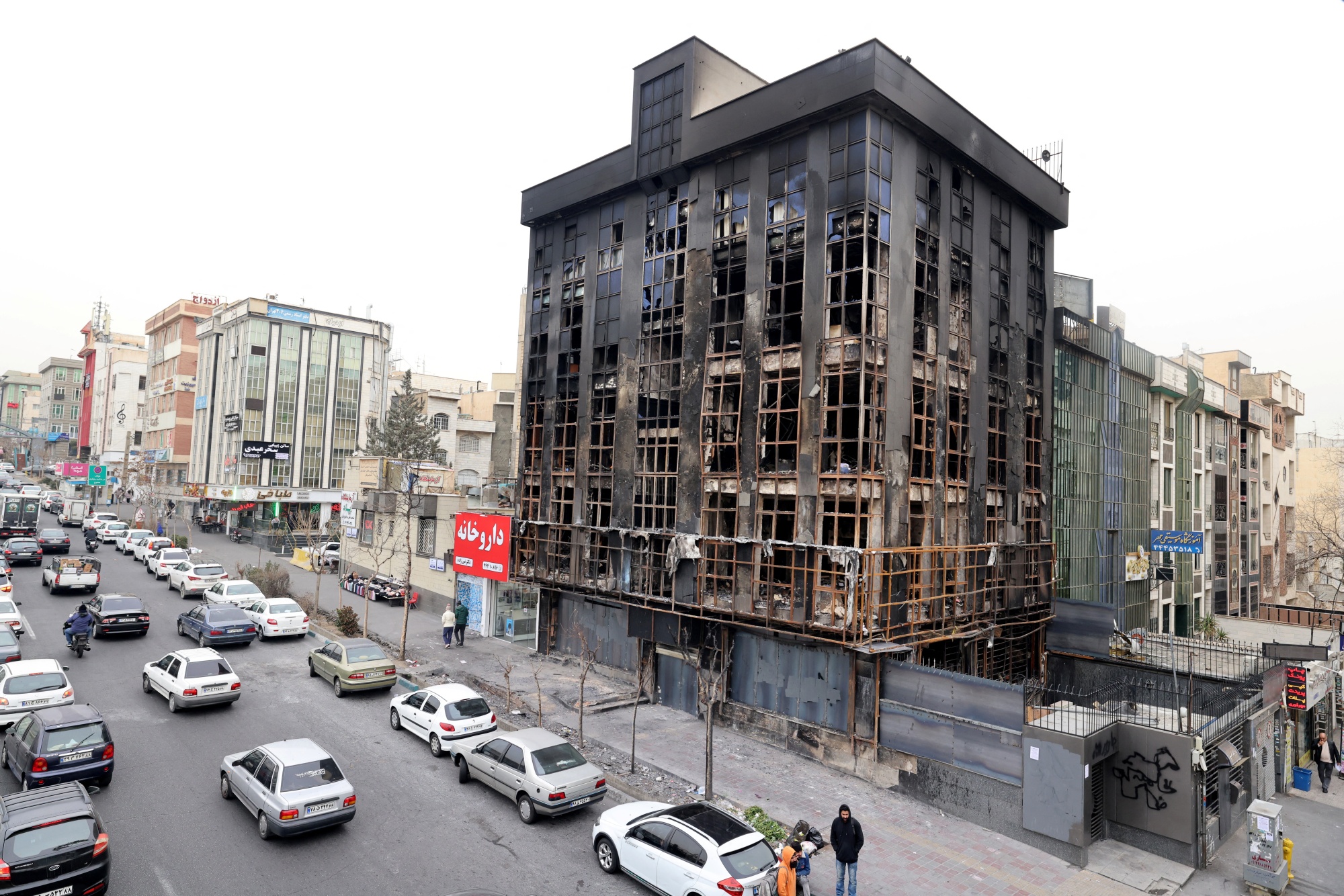 People walk past a building destroyed during public protests in Tehran on Jan. 19. Photographer: Atta Kenare/AFP/Getty Images