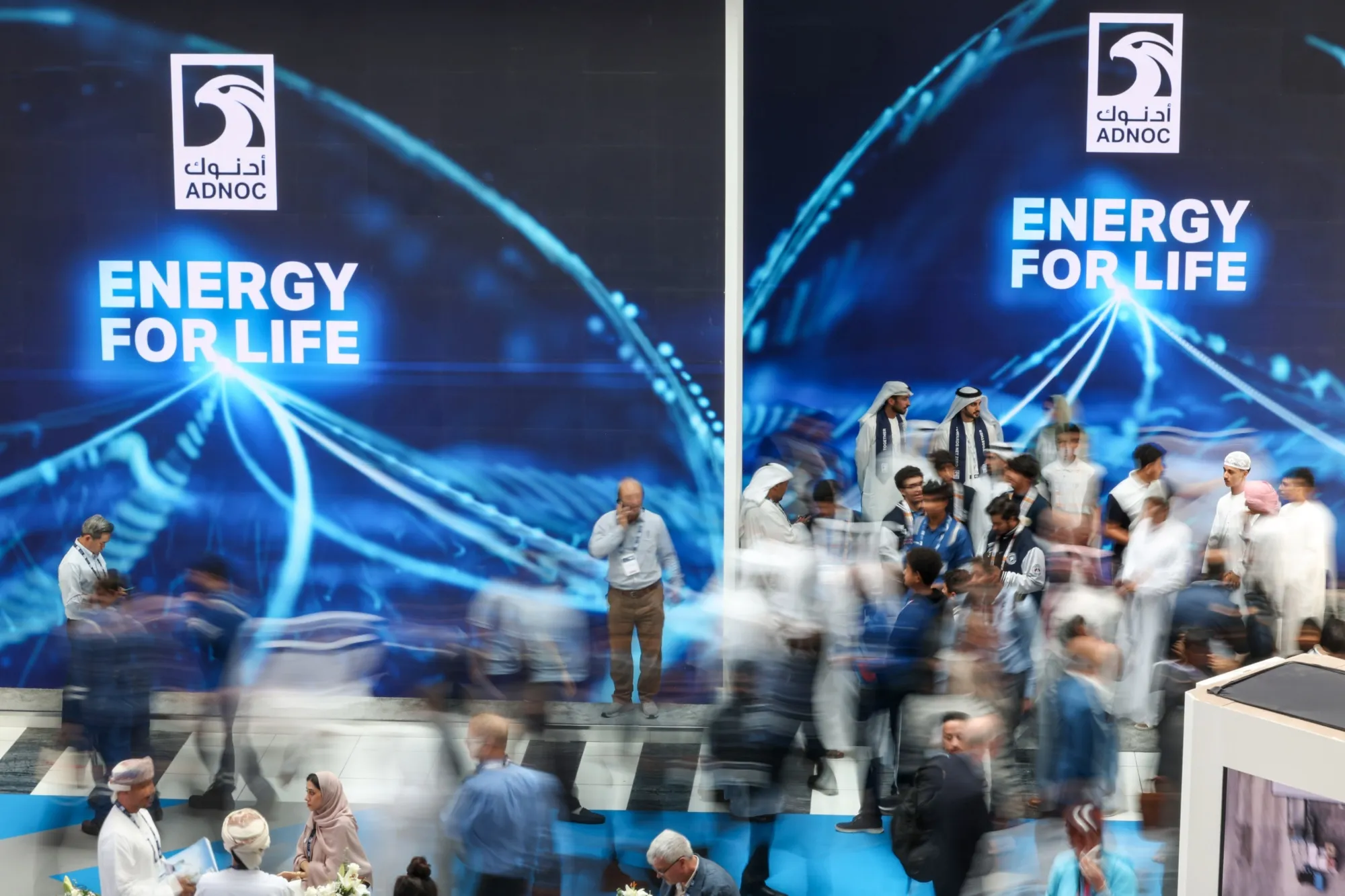Attendees pass signage for Abu Dhabi National Oil Co. (ADNOC) in the venue halls on day two of the Abu Dhabi International Petroleum Exhibition and Conference (ADIPEC) in Abu Dhabi, United Arab Emirates.
